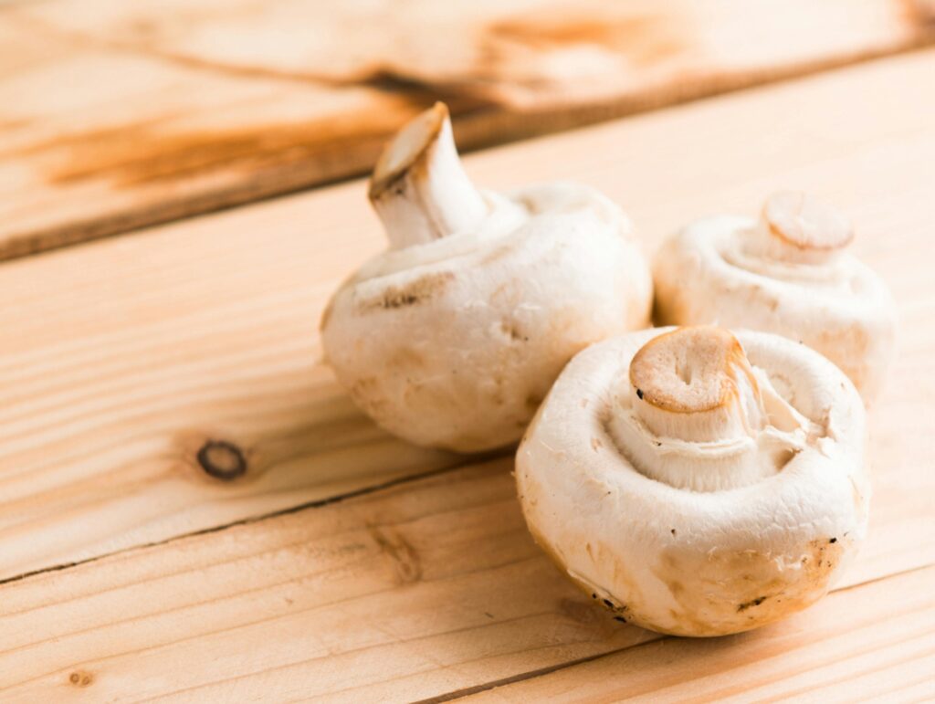 Fresh white mushrooms on a wooden table, showcasing natural textures and earthy tones.